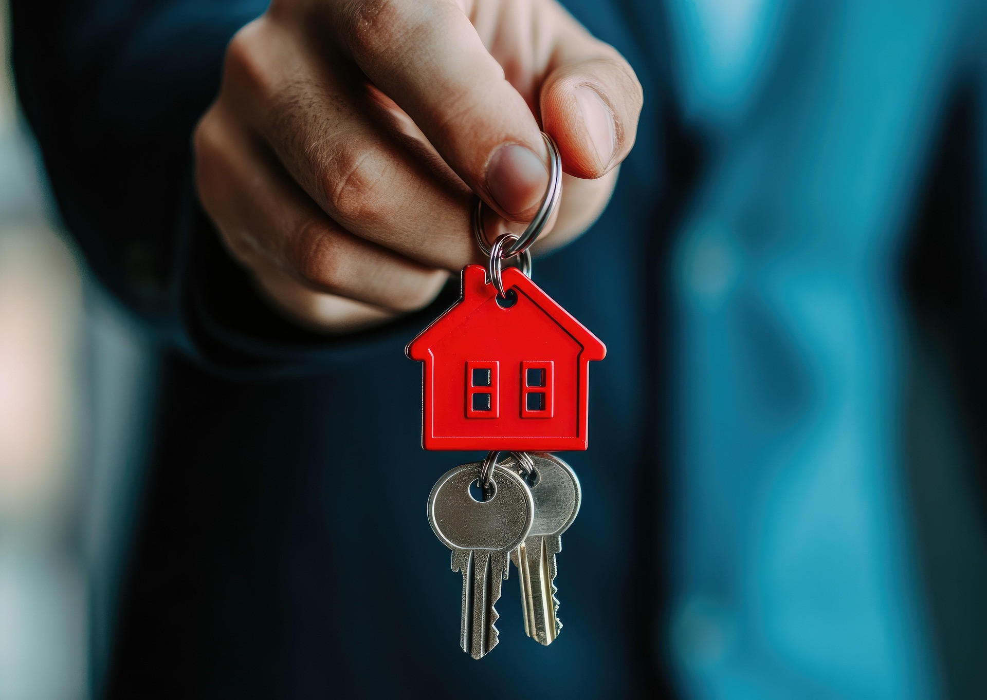 A hand holds a bunch of keys secured onto a red keyring in the shape of a house