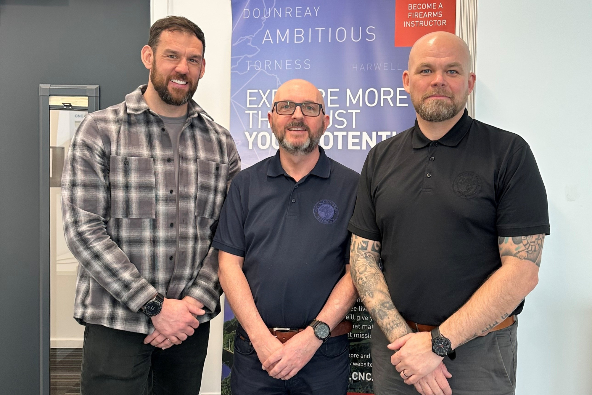 Ben Gallagher, Colin Longstaff and Darren Adams are pictured in a line in front of a pop-up CNC banner. Ben is wearing a checked jacket while Colin and Darren are in dark polo shirts. All are smiling.
